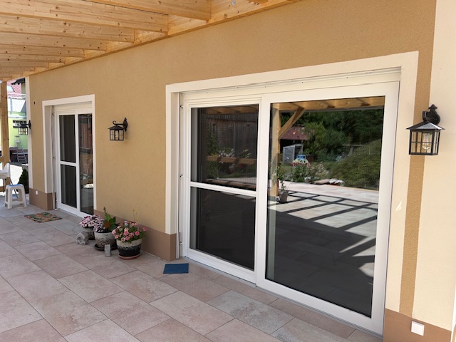 Blick von rechts auf eine doppelte Terrassenglastüre mit weißen Rahmen und Insektenschutzgitter.
