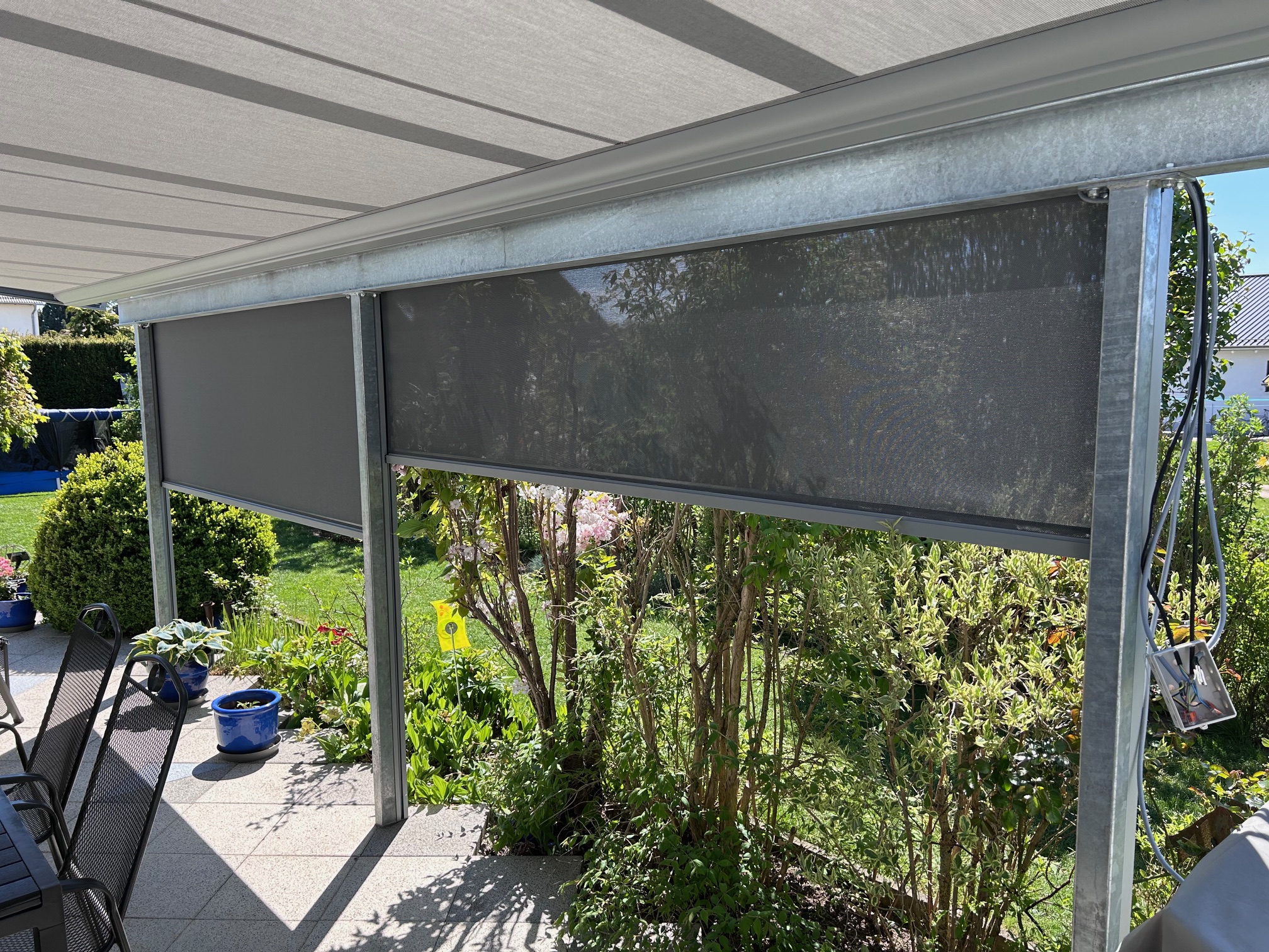 Blick von rechts auf ein heruntergelassenes Markisenteil im Garten an der einer Terrasse.