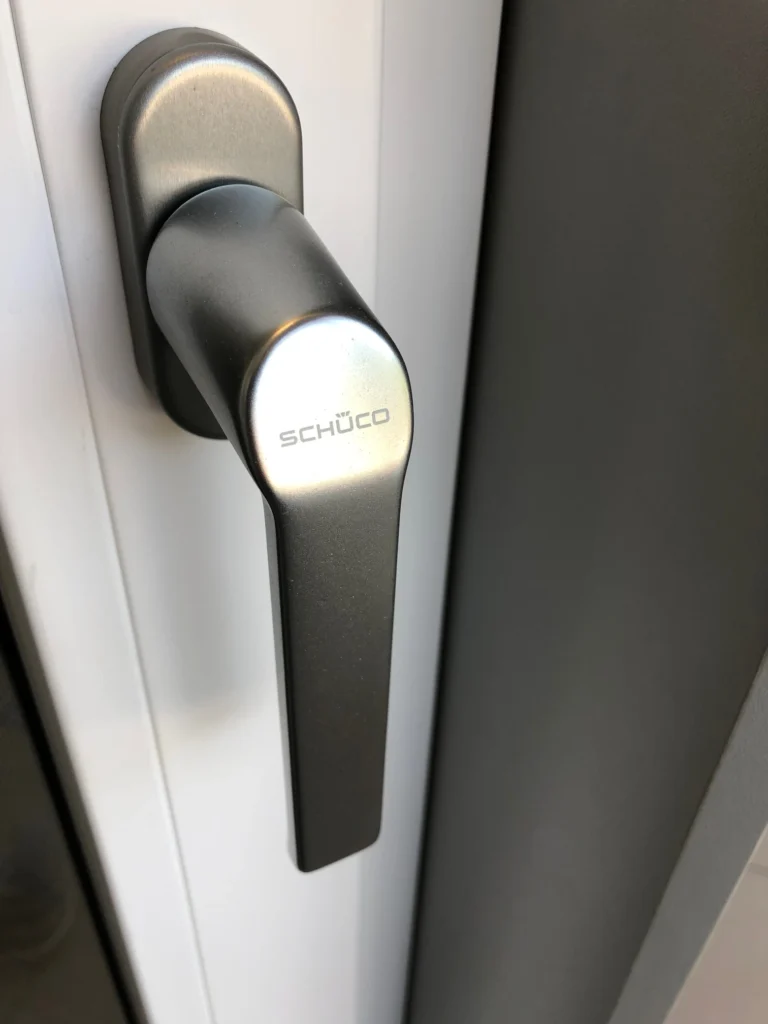Ein grauer Fenstergriff auf einen weißen Rahmen.
