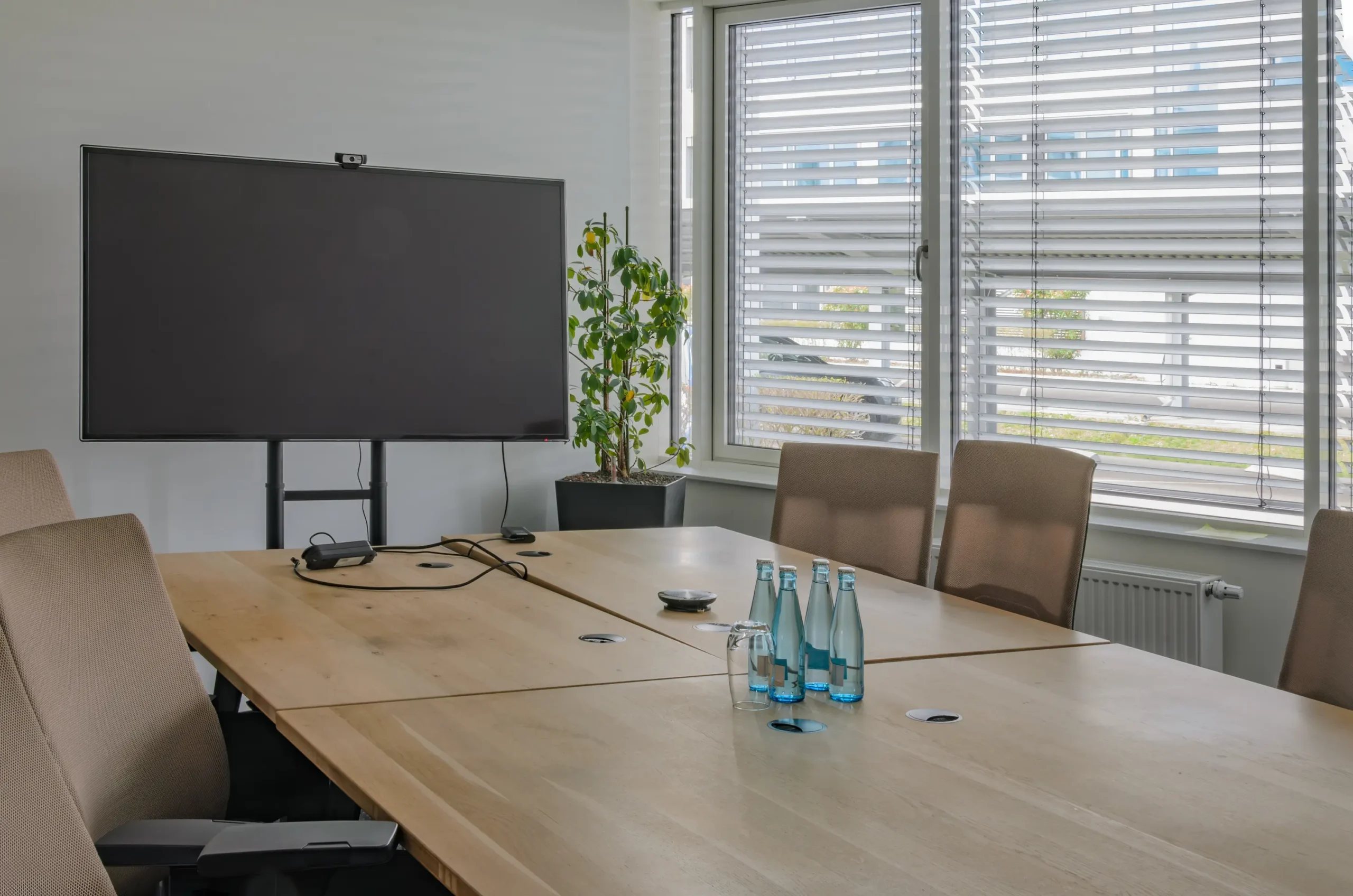 Ein Besprechungsraum mit Smartboards und Fenstern im Hintergrund bei denen die Innenjalousien geschlossen, jedoch gekippt sind.