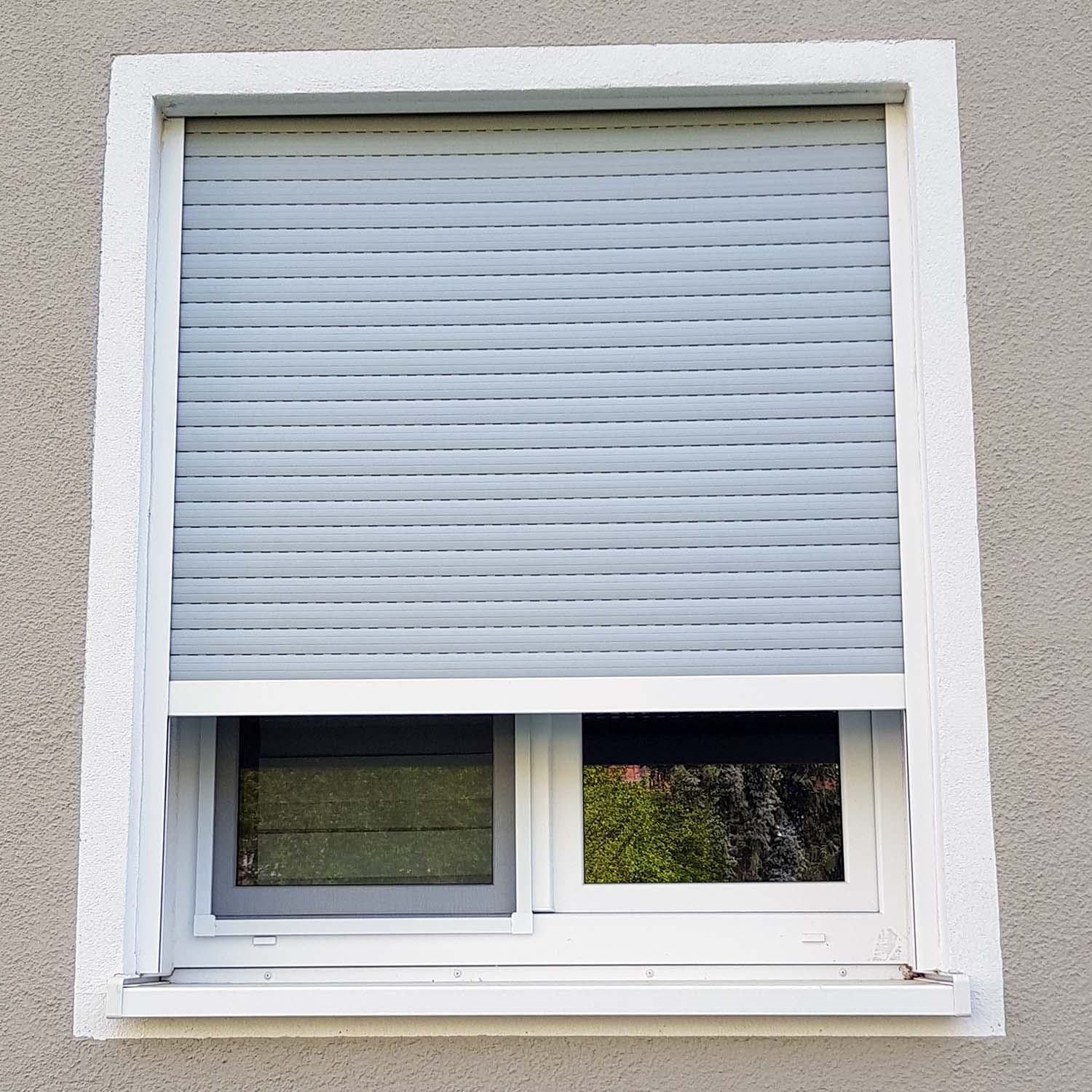 Ein fast geschlossener hellgrauer Rollo am geschlossenen Fenster.