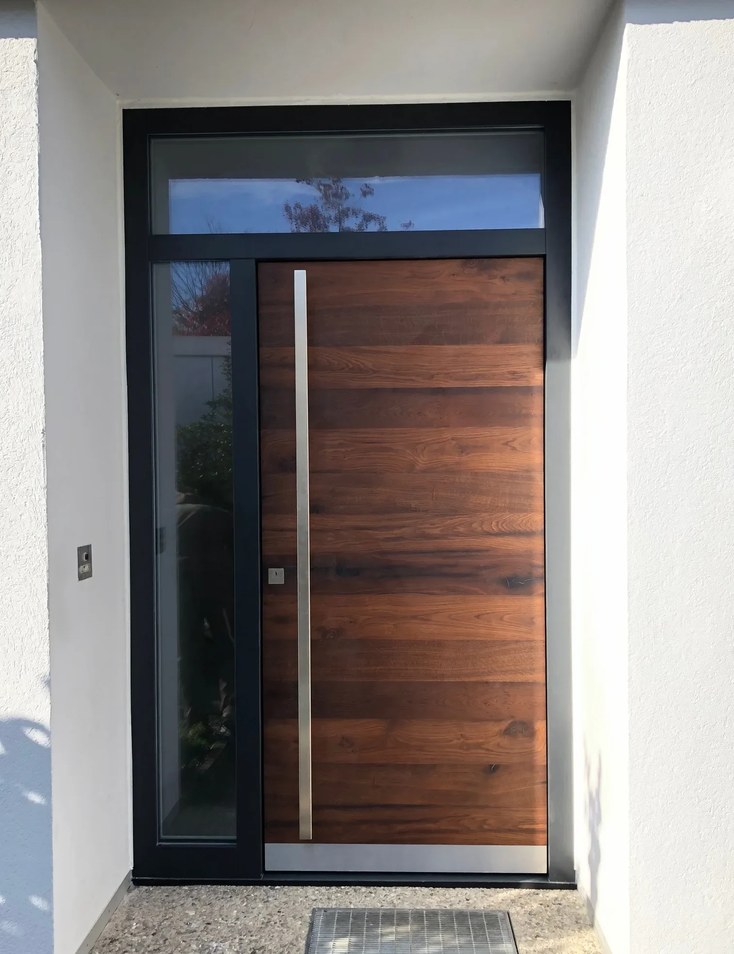 Eine Hautüre mit einen dunklen Holz als Türblatt. oben und links von der Haustüre befinden sich Glaselemente.